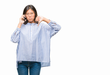 Young asian woman speaking on the phone over isolated background with angry face, negative sign showing dislike with thumbs down, rejection concept