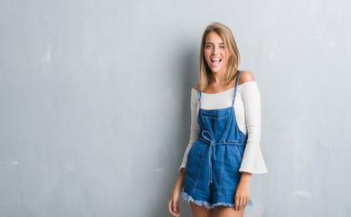 Beautiful young woman standing over grunge grey wall winking looking at the camera with sexy...