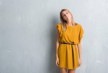 Beautiful young woman standing over grunge grey wall wearing a dress making fish face with lips, crazy and comical gesture. Funny expression.