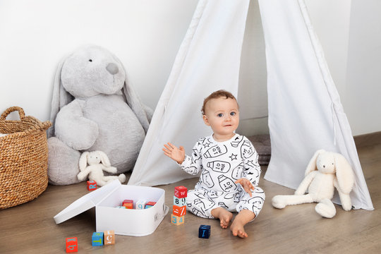Cute toddler sitting on playroom floor playing with blocks