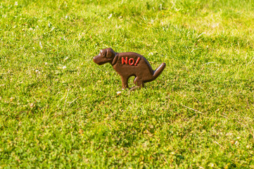 Metal sign of dog, placed on a green lawn, forbidding dogs to defecate on the lawn. Dog walking is prohibited.