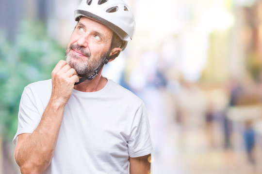 Middle age senior hoary cyclist man wearing bike safety helment isolated background with hand on chin thinking about question, pensive expression. Smiling with thoughtful face. Doubt concept.