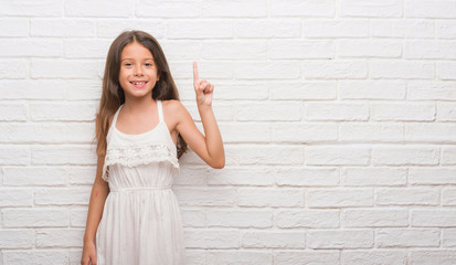 Young hispanic kid over white brick wall showing and pointing up with finger number one while smiling confident and happy.