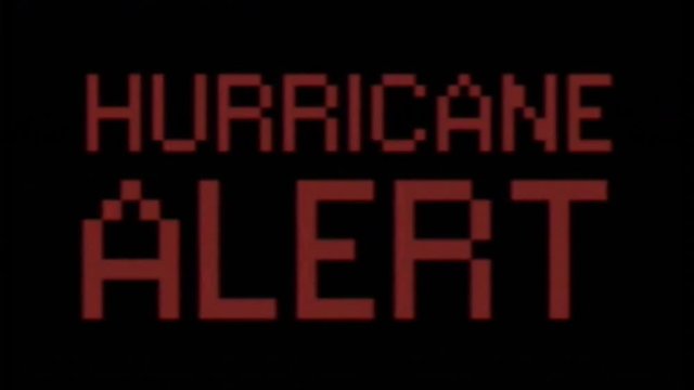 Analog VHS tape distortion: a flashing text with the words Hurricane Alert. Red on black, blocky 8-bit characters, faded color tone.

