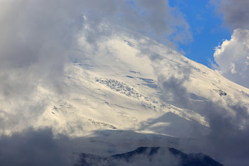The western peak of Mount Elbrus, the slope with snow is visible through the clouds. Mountain range in the North Caucasus in Russia.