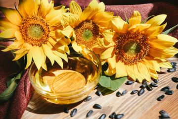 Obraz na płótnie Canvas Sunflower oil with yellow flowers with black seeds on wooden background with sunshine