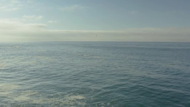 Aerial pullback over the waves and rocks of a cliff on the beach.
