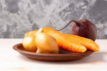Onions, carrots and beetroot in a clay plate. Copy space. Preparing fresh vegetables for cooking