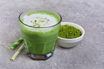 Organic green matcha tea latte in glass and powder in white bowl with cocktail straw