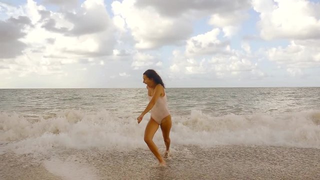 slow motion , slender girl running away from ocean waves from the water on the beach