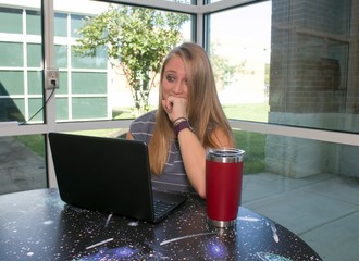 A young woman gazes at her lap top computer in a library.