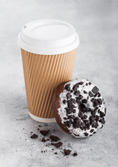 Cardboard coffee cup with black cookies doughnut on stone kitchen table background. Cafe drink and snack.