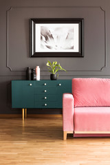 Poster above green cupboard in grey loft interior with pink couch on wooden floor. Real photo