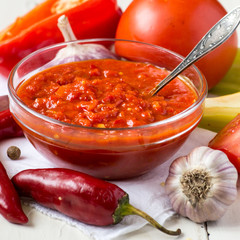 Georgian Adjika sauce in a transparent glass bowl, next to the ingredients for its preparation on an old table. 