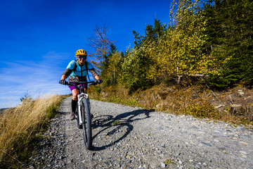 Fototapeta premium Cycling, mountain bikeing woman on cycle trail in autumn forest. Mountain biking in autumn landscape forest. Woman cycling MTB flow uphill trail.