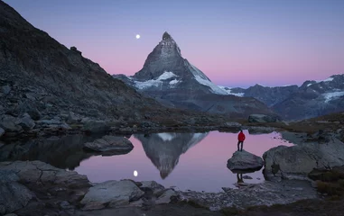 Foto auf Acrylglas Matterhorn Wanderer auf einem Felsen im Riffelsee im Morgengrauen mit Blick auf das Matterhorn.