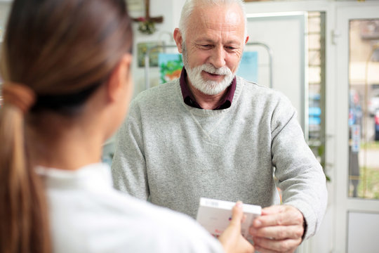Medicine, pharmaceutics, health care and people concept - Young female pharmacist giving medications to smiling senior male customer