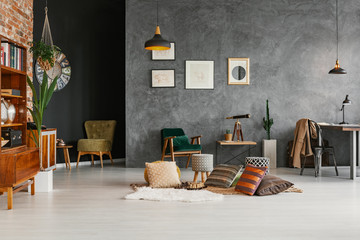 Chess placed on floor with rugs and cushions in dark retro apartment interior with posters on...