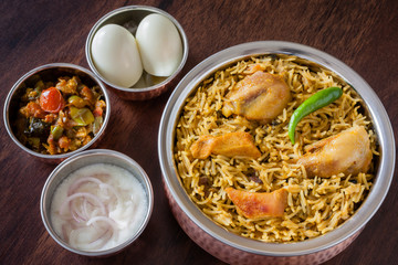 Chicken biryani top view - Overhead view from the top of delicious Indian chicken biryani served  in authentic copper utensils with traditional sides, egg, raita and gravy. Natural light used.
