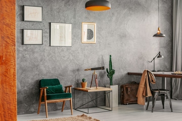Living room interior with posters on raw grey wall, green retro armchair, end table with telescope...
