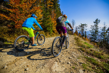Mountain biking woman and man riding on bikes at sunset mountains forest landscape. Couple cycling...