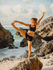 Young sporty woman practicing yoga on the ocean beach. Yoga at sunset