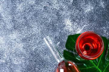 Wine in a wineglass, a bottle and a tropical leaf. Top view. Wine drink on a gray background. Copy space.