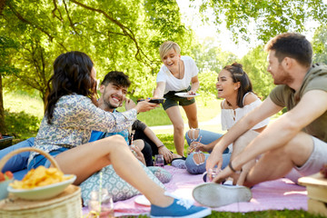 friendship and leisure concept - group of happy friends with non alcoholic drinks and food at picnic in summer park