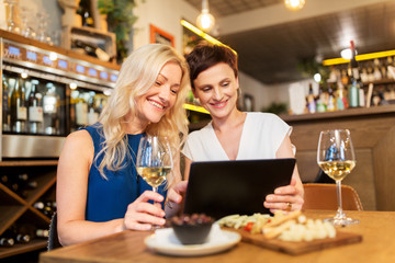 leisure, technology and lifestyle concept - happy women with tablet pc computer at wine bar or restaurant