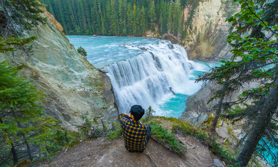 A man sitting on a ground looking at Wapta falls in Canada