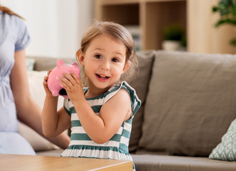 savings and finances concept - happy little girl with piggy bank at home