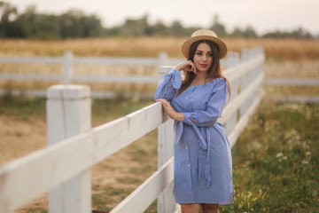 Pregnant woman in hat stand near the fance. farm. Background of field