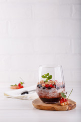 Chia pudding with fresh currant berries in glass on white table.