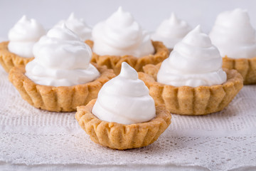 Shortcrust tartlets with jam and Italian meringue on white.
