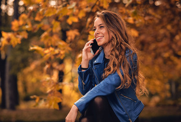 Cute girl using cellphone in park with autumn colors.