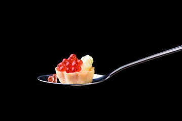 Tartlet with red caviar on a tablespoon on a black background