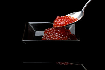 Red Caviar in a spoon over black background with reflection