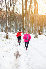 Fototapeta na wymiar Playful young couple running through a snow covered forest. Active and healthy lifestyle concept.