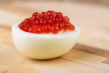 Close up. One half of chicken egg with red caviar on a wooden background