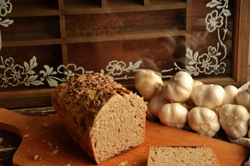 Wholemeal bread spelled on a wooden board. Garlic lying in the background