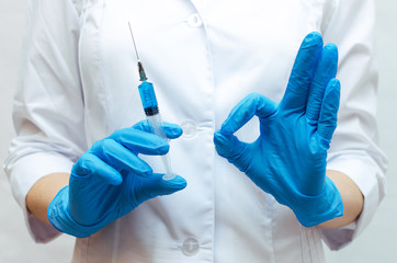 Syringe with a blue medical drug and doctor hand with showing an Okay sign.