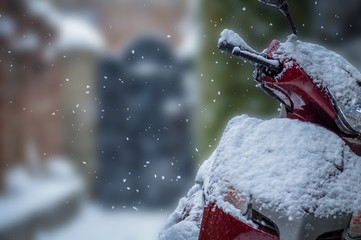 A scooter parked outside a house during snowfall with a shallow depth of field