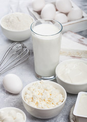 Fresh dairy products on white table background. Glass of milk, bowl of sour cream and cottage cheese and eggs in wooden box. Steel whisk.