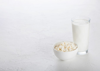 Glass of milk and bowl of cottage cheese on white stone kitchen table background.Space for text