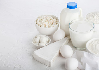 Obraz na płótnie Canvas Fresh dairy products on white table background. Glass of milk, bowl of sour cream, cottage cheese and baking flour and mozzarella. Eggs and cheese. Small plastci bottle of milk.
