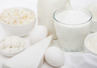 Fresh dairy products on white table background. Glass of milk, bowl of sour cream, cottage cheese and baking flour and mozzarella. Eggs and cheese.