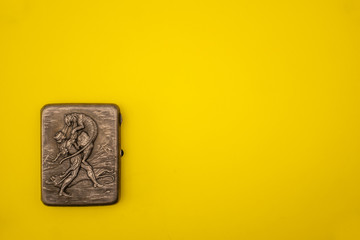 Antique silver cigarette case on a yellow background.