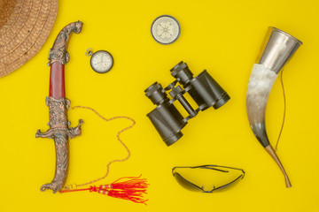 Horn for drinking wine.Traveler's things: hat, binoculars, glasses, compass, watch, knife, camera, flask on a yellow background.