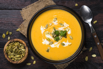 Pumpkin soup on dark wooden table top view.