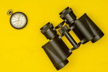 Traveler's items: antique pocket watch and binoculars depicted on a yellow background.